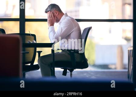 Un uomo d'affari maturo che lavora su un computer portatile seduto al tavolo della sala riunioni Foto Stock