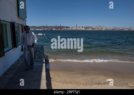 Un uomo ha visto camminare vicino alle rive del fiume Tejo nella zona portuale di Almada. Situata sulla riva sud del fiume Tejo, Almada è il miglior punto panoramico della città di Lisbona, con il castello, l'ascensore panoramico di Boca do vento e la statua del Cristo Re costruita nel 1959, sono utilizzati come punti di osservazione. Foto Stock