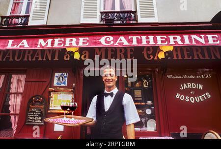 CAMERIERE DI PARIGI MONTMARTRE cameriere francese maschio in stile retrò, in tipica uniforme bianca e nera da cameriere con papillon, che serve bicchieri di vino rosso all'aperto su vassoio presso il rinomato ristorante la Mere Catherine Boulevard Montmartre Parigi Francia Foto Stock