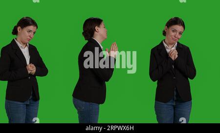 Primo piano di un impiegato aziendale che fa le mani di preghiera firmano sulla macchina fotografica, pregando dio chiedendo fortuna. Persona religiosa spirituale in silenzio sullo sfondo verde, speranza e fede. Foto Stock