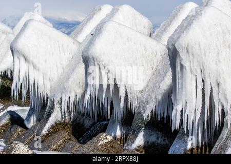 Blocchi di cemento ricoperti di ghiaccio mentre infrangono le onde sulla spiaggia giapponese in inverno. Isola di Hokkaido, Giappone Foto Stock