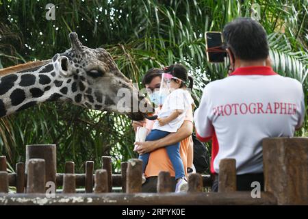 200706 -- SINGAPORE, 6 luglio 2020 Xinhua -- i visitatori che indossano maschere facciali danno da mangiare a una giraffa nello zoo di Singapore il 6 luglio 2020. Lo zoo di Singapore ha riaperto al pubblico lunedì dopo l'allentamento delle misure di confinamento nella lotta contro la pandemia di COVID-19. Foto di Then Chih Wey/Xinhua SINGAPORE-COVID-19-ZOO-REOPENING PUBLICATIONxNOTxINxCHN Foto Stock