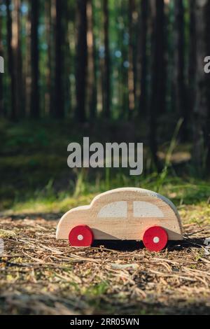 Macchinina giocattolo in legno su sfondo verde della foresta. Eco-car Concept World auto giorno libero veicolo elettrico ambiente trasporto auto elettrico. Ibrido elettrico. Motore sostenibile. Zero emissioni di CO2 per la consapevolezza naturale e il concetto di inquinamento ambientale verde Foto Stock