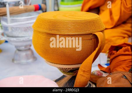 Una ciotola di elemosina di metallo ricoperta da un panno d'arancio dorato per ricevere cibo da laici e persone che credono nel buddismo. Foto Stock
