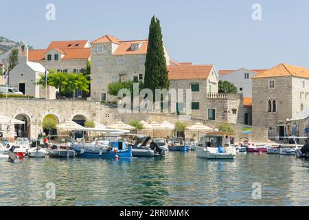 Croazia Island Brac Bol porto città portuale ormeggi sul lungomare barche a motore caffetteria ristorante ombrelloni ufficio turistico Big Blue Sports Shop Chiesa Foto Stock