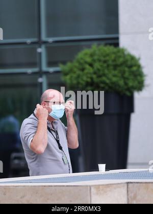 200820 -- PARIGI, 20 agosto 2020 -- Un uomo si toglie la maschera facciale mentre si riposa fuori da un edificio di uffici nella zona commerciale la Defense vicino a Parigi, in Francia, 20 agosto 2020. I lavoratori francesi dovrebbero indossare maschere in tutti i luoghi di lavoro collettivi come parte di un piano governativo per contenere un rimbalzo allarmante nelle infezioni da coronavirus, ha annunciato martedì il ministro del lavoro Elisabeth Borne. FRANCIA-PARIGI-COVID-19 GaoxJing PUBLICATIONxNOTxINxCHN Foto Stock
