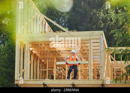 Uomo, costruttore, operaio che costruisce una casa in legno nella foresta, con il sole, in estate. Foto Stock