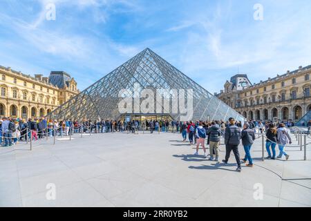 PARIGI, FRANCIA - 16 APRILE 2023: Affollato cortile del Museo Louver con monumentale piramide di vetro, Parigi, Francia. Foto Stock