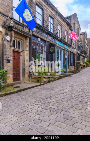 Il grazioso villaggio di Haworth, vicino a Keighley nei Pennines, West Yorkshire. Questa caratteristica strada ripida è Main Street, fiancheggiata da incantevoli cottage. Foto Stock