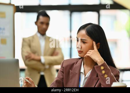 Dipendente donna stressata insoddisfatta dei risultati di lavoro e del capo rigoroso che sta in piedi sullo sfondo Foto Stock