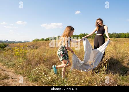 Madre e figlia si stanno preparando per un picnic nel campo estivo, spargendo una coperta sull'erba Foto Stock