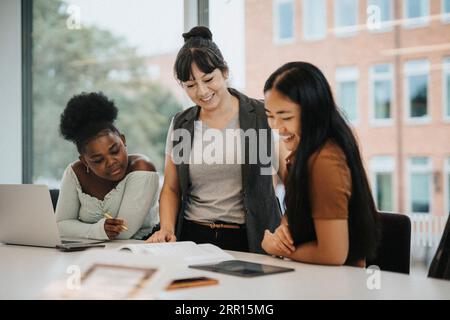 Professoressa sorridente che spiega studenti multirazziali a tavola all'università Foto Stock