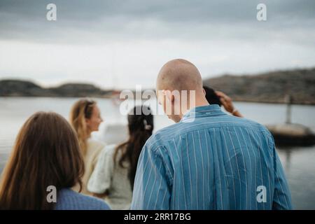 Vista posteriore di uomo e donna che si divertono con gli amici vicino al lago Foto Stock