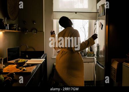 Giovane donna spensierata che indossa accappatoio che balla in cucina a casa Foto Stock