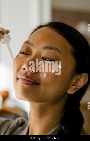Donna sorridente che applica la crema sul viso Foto Stock