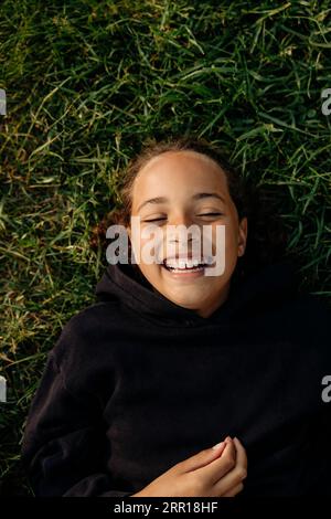 Ragazza felice che ride mentre si sdraiava sull'erba al campo estivo Foto Stock