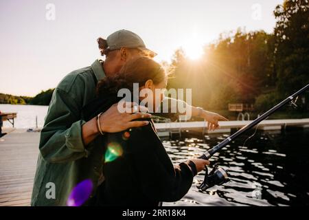 Consigliere maschile con una ragazza che pesca sul molo vicino al lago al campo estivo Foto Stock