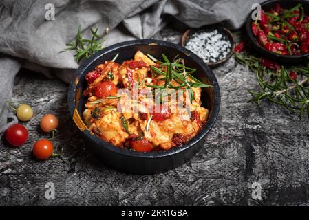 Ravioli, con pomodori ciliegini, guarniti con rosmarino, in una ciotola nera su fondo di legno grigio. Vista dall'alto Foto Stock