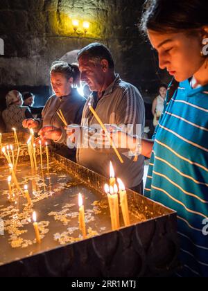 Sevan, Armenia - 25 agosto 2023: I parrocchiani accendono le candele nella chiesa Surp Arakelots nel monastero di Sevanavank. Il monastero di Sevan fu fondato nel 874 Foto Stock