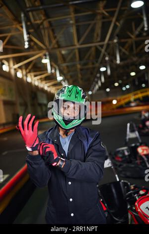 ambizioso pilota di sport motoristici afro-americani indossando guanti e in piedi vicino al go-kart Foto Stock