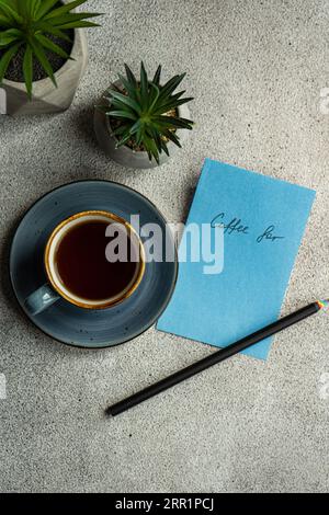 Vista dall'alto della tazza di caffè vicino alle piante in vaso e nota con una matita posizionata su un tavolo grigio Foto Stock