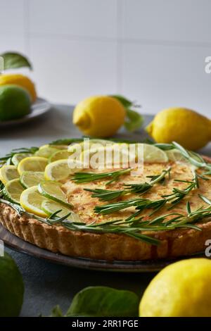 Torta al limone rotonda decorata con fette di limone e ciuffi di rosmarino sul tavolo in cucina Foto Stock