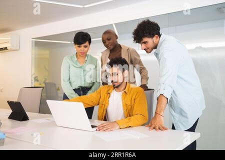 Gruppo di colleghi multirazziali che si riuniscono al tavolo e lavorano al progetto utilizzando un computer portatile in un ufficio moderno Foto Stock