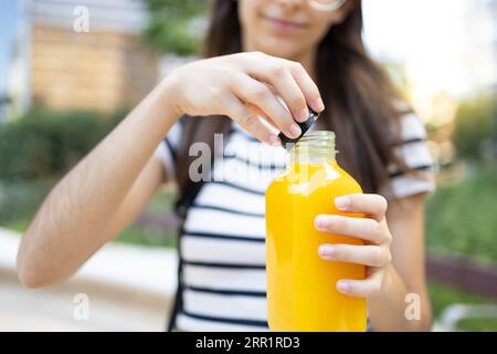 Risolvi una bottiglia di succo d'arancia fresca sorridente mentre ti trovi in città su uno sfondo sfocato Foto Stock