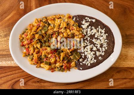 Vista dall'alto dell'appetitoso uovo fritto con pomodori peperoncino verde e fagioli neri tortillas di mais condite con formaggio grattugiato servite su marmo bianco PL Foto Stock