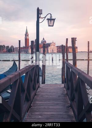 Magnifica vista del molo in legno contro l'antico edificio della Chiesa del Santissimo Redentore e cielo colorato al tramonto a Venezia Foto Stock