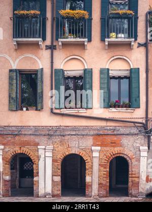 Pittoresco esterno del vecchio e colorato edificio con fiori su finestre e balconi sopra gli ingressi ad arco sulla strada della città di Venezia Foto Stock