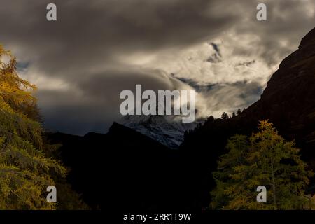 Splendida vista delle verdi colline e delle cime innevate sotto un cielo nuvoloso in un pomeriggio buio e sobrio Foto Stock