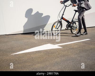 Vista laterale di una persona anonima corta in bicicletta lungo la strada asfaltata con puntatore vicino alla parete bianca Foto Stock