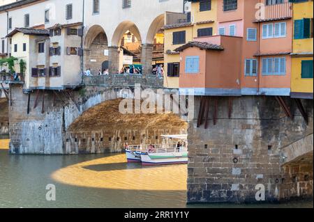 La folla si ferma per ammirare il fiume Arno sotto i grandi archi mentre attraversa il ponte medievale più antico (Ponte Vecchio) con il suo romano Foto Stock