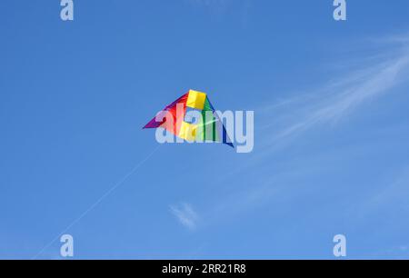 Un aquilone acrobatico colorato con colori arcobaleno nel cielo blu Foto Stock