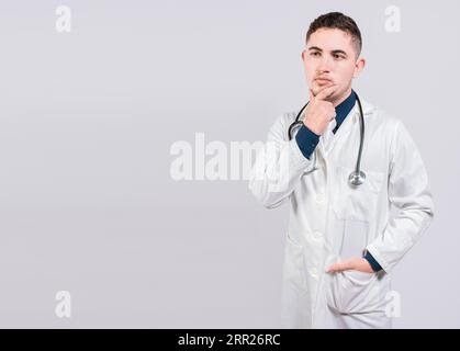 Un medico pensivo che guarda in alto. Giovane medico che pensa e guarda in alto isolato, Dottore che pensa con la mano sul mento Foto Stock