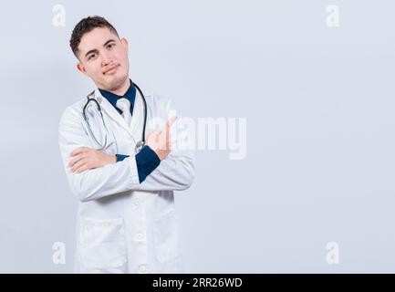 Sorridente medico latino che punta il dito in uno spazio isolato. Giovane medico che si presenta in uno spazio vuoto. Un medico che indica uno spazio bianco isolato Foto Stock