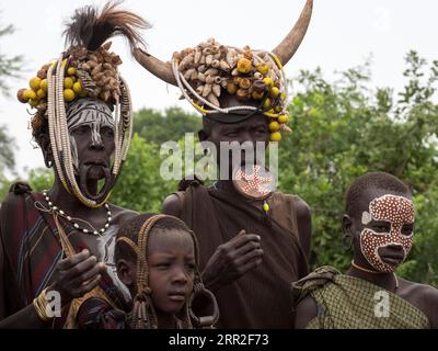 Le donne e i bambini della tribù dei Mursi con copricapo e piastra a labbro, Etiopia Foto Stock