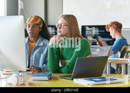 Studentesse che lavorano con la presentazione online al computer mentre sono sedute alla scrivania in classe Foto Stock