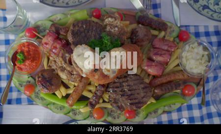 Abbondante assortimento di piatti greci, salsicce di carne, patatine fritte, pancetta, salse, e composizione fritta vista dall'alto. Varietà di cucina malsana Foto Stock