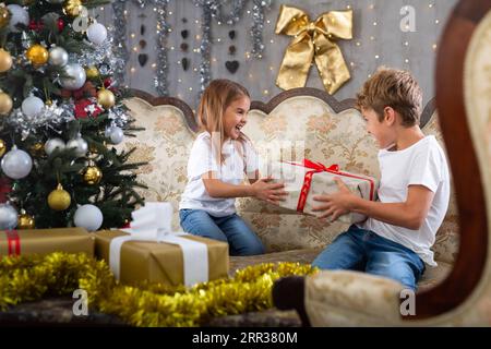 Bambina e ragazzo in casa con regalo in studio con interni natalizi Foto Stock