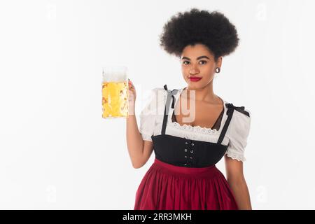 una cameriera afroamericana all'octoberfest in costume autentico con birra artigianale tazza su bianco Foto Stock