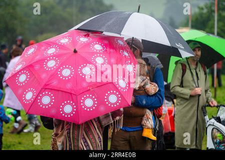 Una famiglia si rifugia sotto gli ombrelli sotto la pioggia e il fango. Green Man Festival, Brecon, Galles, Regno Unito, 2023. Foto: Rob Watkins Foto Stock