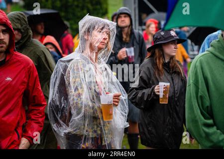 Una donna di mezza età bagnata con birra sotto pioggia e fango. Green Man Festival, Brecon, Galles, Regno Unito, 2023. Foto: Rob Watkins Foto Stock