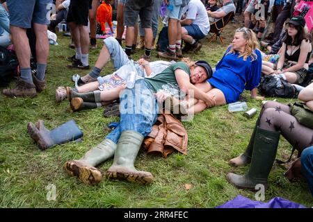 Un uomo fa un pisolino sul giro del suo partner, frequentatori del festival di mezza età al Green Man Festival, Brecon, Galles, Regno Unito, 2023. Foto: Rob Watkins Foto Stock