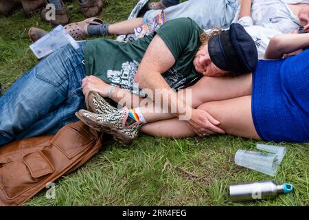 Un uomo fa un pisolino sul giro del suo partner, frequentatori del festival di mezza età al Green Man Festival, Brecon, Galles, Regno Unito, 2023. Foto: Rob Watkins Foto Stock