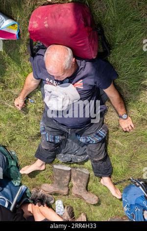 Un anziano di mezza età fa un pisolino al sole e mette i suoi pozzi fangosi sull'erba al Green Man Festival di Brecon, Galles, Regno Unito, 2023. Foto: Rob Wat Foto Stock