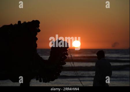 201206 -- PECHINO, 6 dicembre 2020 -- la foto scattata il 4 dicembre 2020 mostra la sagoma di un cammello e del suo proprietario in attesa di clienti in spiaggia durante il tramonto nella città portuale del Pakistan meridionale di Karachi. XINHUA FOTO DEL GIORNO AhmadxKamal PUBLICATIONxNOTxINxCHN Foto Stock