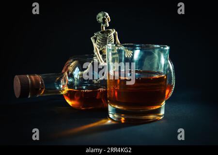 Lo scheletro umano è seduto con una bottiglia e un bicchiere di whisky in una stanza buia. Il concetto di lotta contro l'alcolismo. L'alcol uccide. Foto Stock