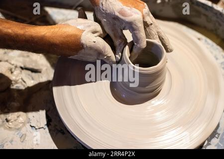 Primo piano delle mani maschili che fanno ceramiche usando l'argilla sulla ruota di un vasaio. Foto Stock